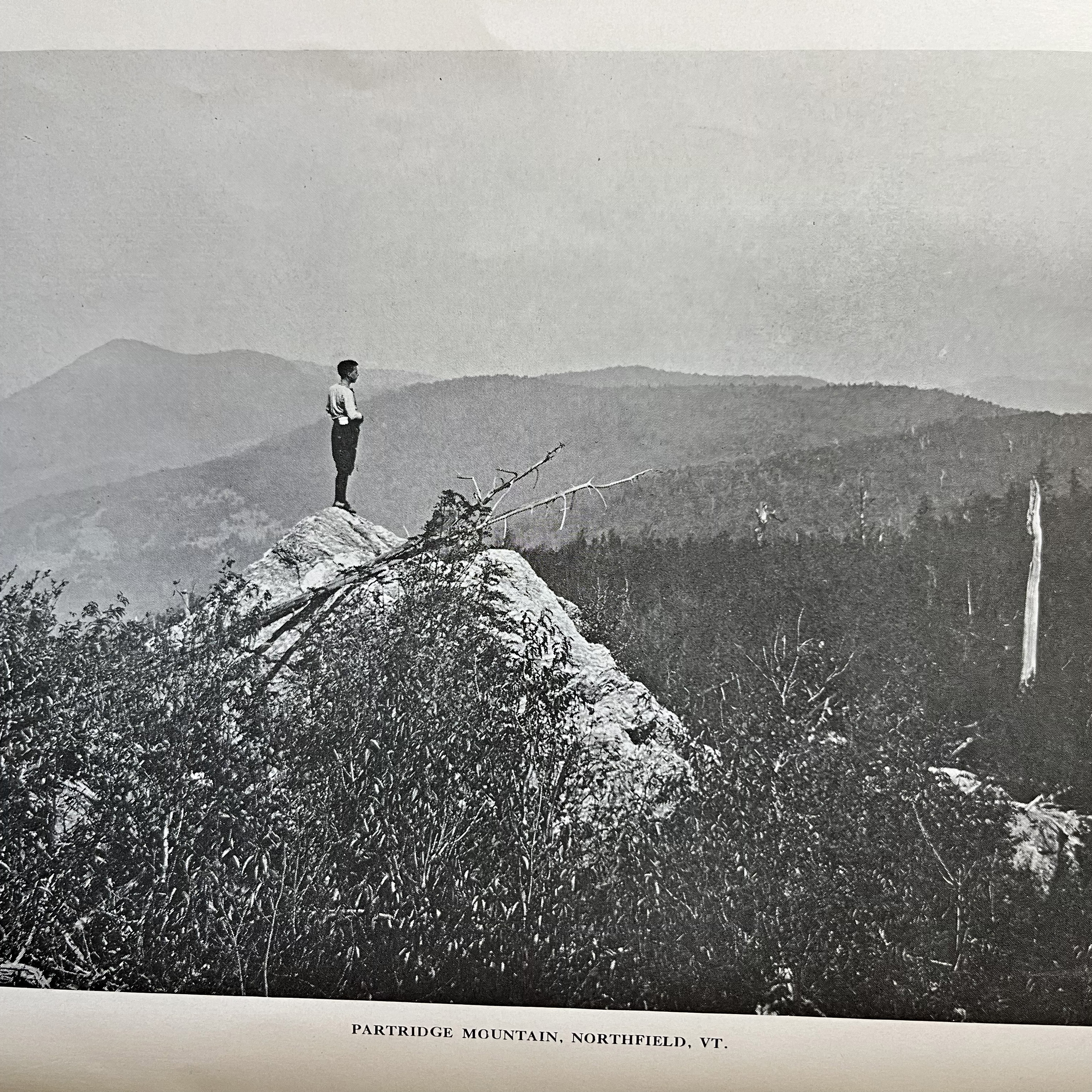 A person stands on a rocky ledge above Partridge Mountain in Northfield, Vermont.