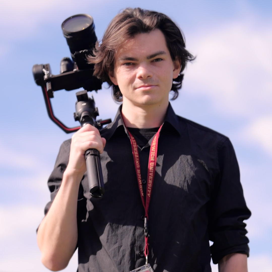 Student holds camera stabilizer outdoors while wearing a Norwich University lanyard.