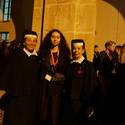 Student poses with two nuns outside a stone building at night.