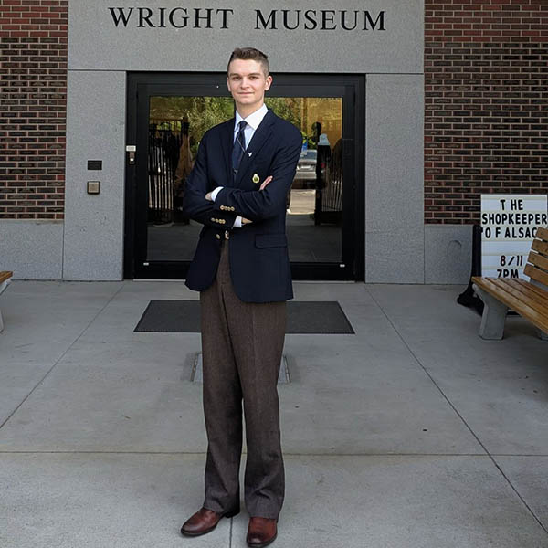 A person in a blazer stands with arms crossed outside the Wright Museum entrance.
